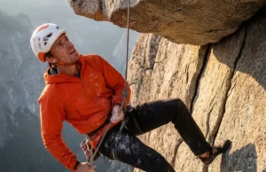 Safe Rope Ascent & The 60-Second Transition Matrix A climber wearing an Arc'teryx jacket and Petzl helmet ascending a fixed rope in free space below a rock roof.