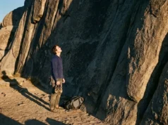 Sociology of Climbing: From Gym Rat to Dirtbag A climber stands at the base of a large granite cliff at sunset, preparing gear for a route.
