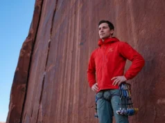 The Wet Rock Rule: Science-Backed Desert Climbing Ethics A professional climber in Arc'teryx gear standing at the base of a red sandstone tower in Indian Creek, contemplating the route with a respectful expression, bathed in soft morning light.