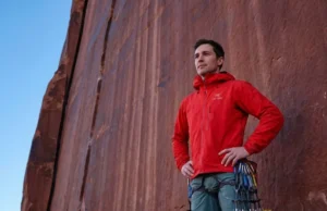 The Wet Rock Rule: Science-Backed Desert Climbing Ethics A professional climber in Arc'teryx gear standing at the base of a red sandstone tower in Indian Creek, contemplating the route with a respectful expression, bathed in soft morning light.