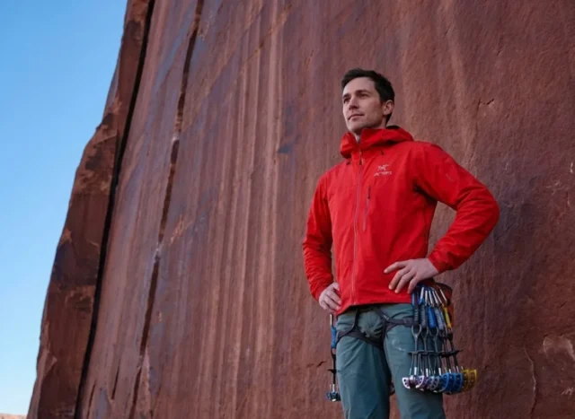 wet-rock-rule-desert-ethics A professional climber in Arc'teryx gear standing at the base of a red sandstone tower in Indian Creek, contemplating the route with a respectful expression, bathed in soft morning light.