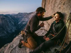 Wilderness First Aid for Climbers: Vertical Field Guide A climber on a high rock ledge performs a medical assessment on their partner during sunset.