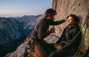 Wilderness First Aid for Climbers: Vertical Field Guide A climber on a high rock ledge performs a medical assessment on their partner during sunset.