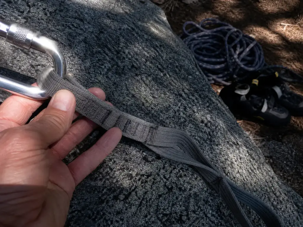 Locking carabiner clipped across two adjacent daisy chain pockets showing the mis-clip failure mode