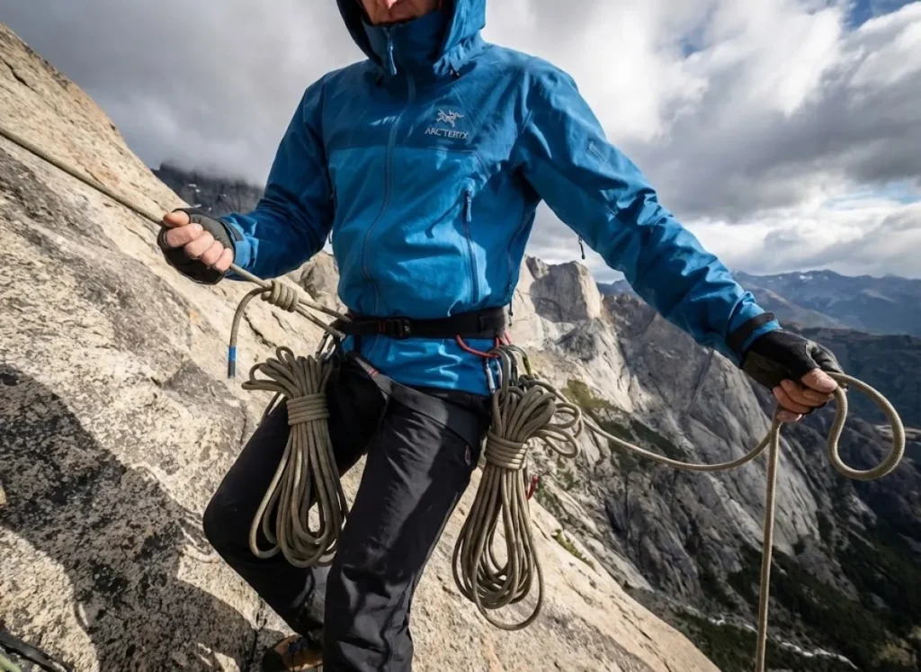 A climber in full Arc'teryx gear rappels in high winds, using the saddlebag technique to manage the ropes which are coiled and clipped to their harness.