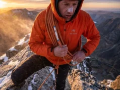Alpine Rope Management: A Strategic Decision Framework Alpinist in an orange Arc'teryx jacket coiling a Petzl rope on a high exposed ridge during a windstorm.