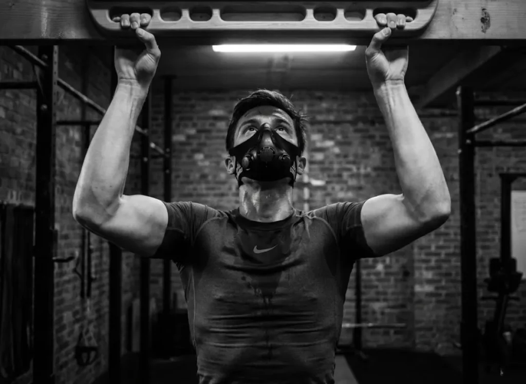 A climber sweating profusely while wearing an elevation training mask and Nike compression gear during a gym workout.