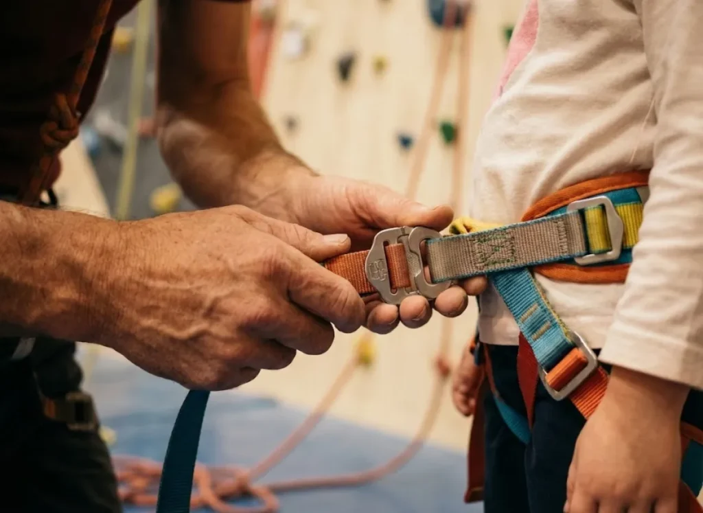 Close up of an adult adjusting a child's climbing harness buckle for safety.