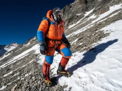 Climbing Aconcagua Guide: 2026 Costs, Route & Readiness A climber in a full down suit ascends the steep Canaleta on Aconcagua near the summit under a dark blue high-altitude sky.