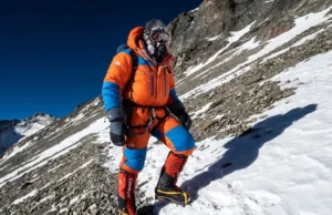 Climbing Aconcagua Guide: 2026 Costs, Route & Readiness A climber in a full down suit ascends the steep Canaleta on Aconcagua near the summit under a dark blue high-altitude sky.
