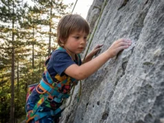Climbing Gear for Kids: From Toddler to Crusher A young child rock climbing outdoors wearing a full-body safety harness.