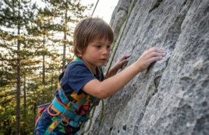 Climbing Gear for Kids: From Toddler to Crusher A young child rock climbing outdoors wearing a full-body safety harness.