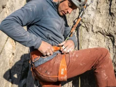 How to Fit a Climbing Harness: The Suspension Audit Close up of a climber adjusting a Petzl Sitta harness at a hanging belay on a limestone cliff.