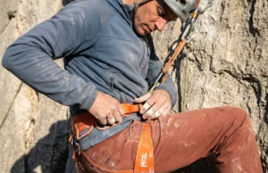 How to Fit a Climbing Harness: The Suspension Audit Close up of a climber adjusting a Petzl Sitta harness at a hanging belay on a limestone cliff.