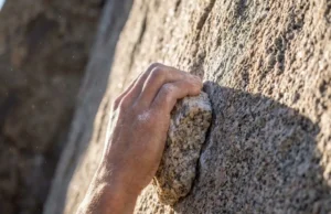 Climbing Rock Types: The Tactical Guide to Grip & Gear Close-up of a rock climber's hand gripping a rough granite edge with visible chalk and rock crystals.