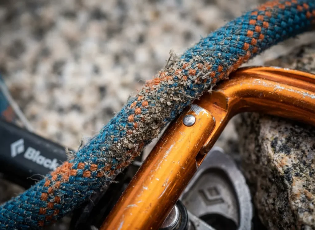 Macro shot of a dirty Sterling Velocity rope grinding against a Black Diamond Camalot carabiner showing dust and wear.