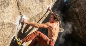 How to Dyno Climbing: Physics, Drills & Safety Climber wearing La Sportiva Solution Comp shoes and Patagonia pants executing a high dynamic move on a granite boulder.