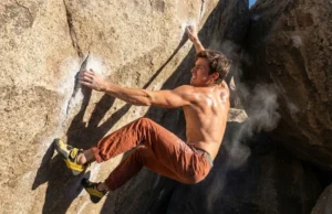 How to Dyno Climbing: Physics, Drills & Safety Climber wearing La Sportiva Solution Comp shoes and Patagonia pants executing a high dynamic move on a granite boulder.
