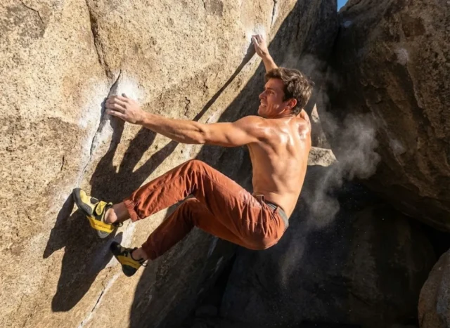 dyno-climbing-physics-drills-safety Climber wearing La Sportiva Solution Comp shoes and Patagonia pants executing a high dynamic move on a granite boulder.
