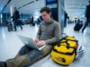 Global Climbing Travel Visa Guide: The 2026 Matrix Climber sitting on airport floor with The North Face duffel bag and Petzl helmet working on Apple MacBook Pro.