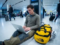Global Climbing Travel Visa Guide: The 2026 Matrix Climber sitting on airport floor with The North Face duffel bag and Petzl helmet working on Apple MacBook Pro.