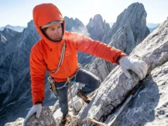 High Altitude Training for Climbers: Science & Protocols A climber wearing an orange Arc'teryx jacket and La Sportiva shoes scaling a high-altitude ridge with snowy peaks in the background.