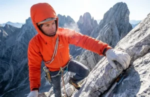 High Altitude Training for Climbers: Science & Protocols A climber wearing an orange Arc'teryx jacket and La Sportiva shoes scaling a high-altitude ridge with snowy peaks in the background.