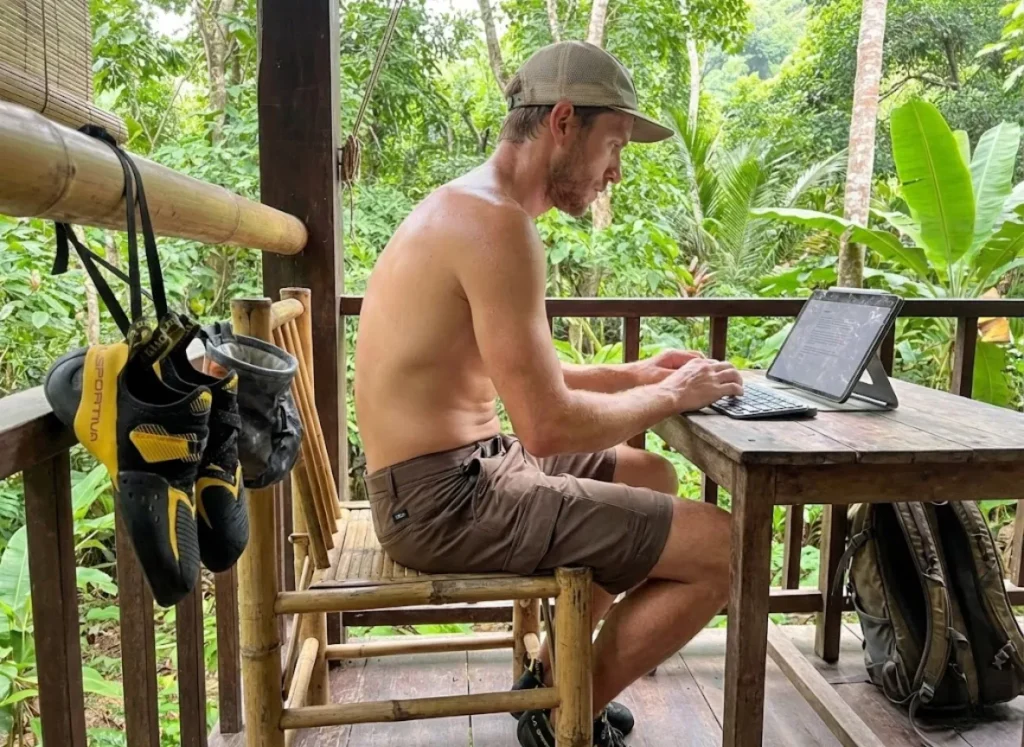 Climber working remotely in Thailand bungalow with Logitech keyboard and La Sportiva climbing shoes drying.
