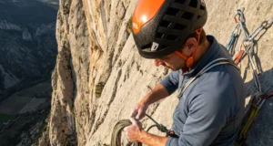 How to Clean a Sport Anchor: Visual Safety Guide Climber securing a Mammut rope at a cliff edge anchor wearing a Petzl helmet and Black Diamond harness.