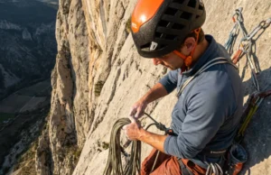 How to Clean a Sport Anchor: Visual Safety Guide Climber securing a Mammut rope at a cliff edge anchor wearing a Petzl helmet and Black Diamond harness.
