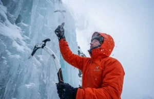 Ice Climbing Grades Explained: Angles, Gear & Conditions Climber on vertical ice wearing Arc'teryx Alpha SV jacket and using Petzl Nomic ice tools.