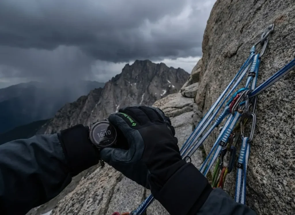 POV of a climber wearing Black Diamond gloves checking a Garmin Fenix watch with storm clouds approaching in the background.