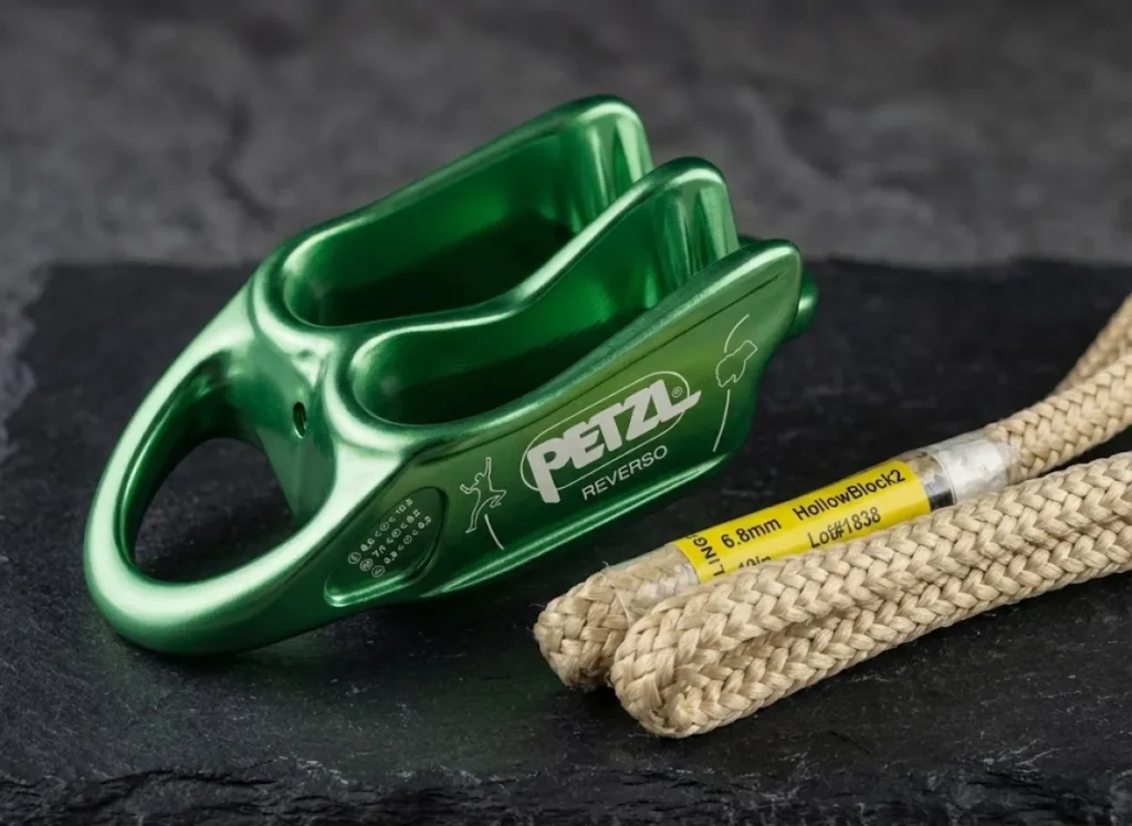 A macro studio photograph of a pristine Petzl REVERSO belay device and a Sterling HollowBlock, highlighting the micro-textures of the metal and heat-resistant fabric.