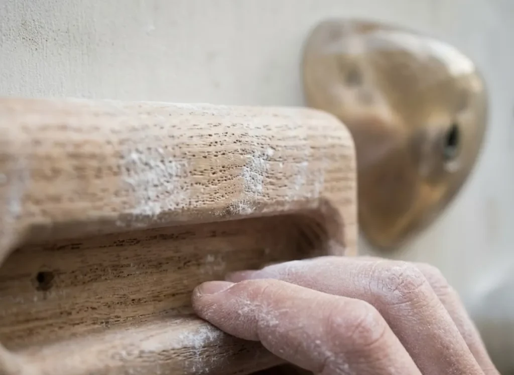 Close-up detail of a wooden hangboard texture with a chalky hand nearby.