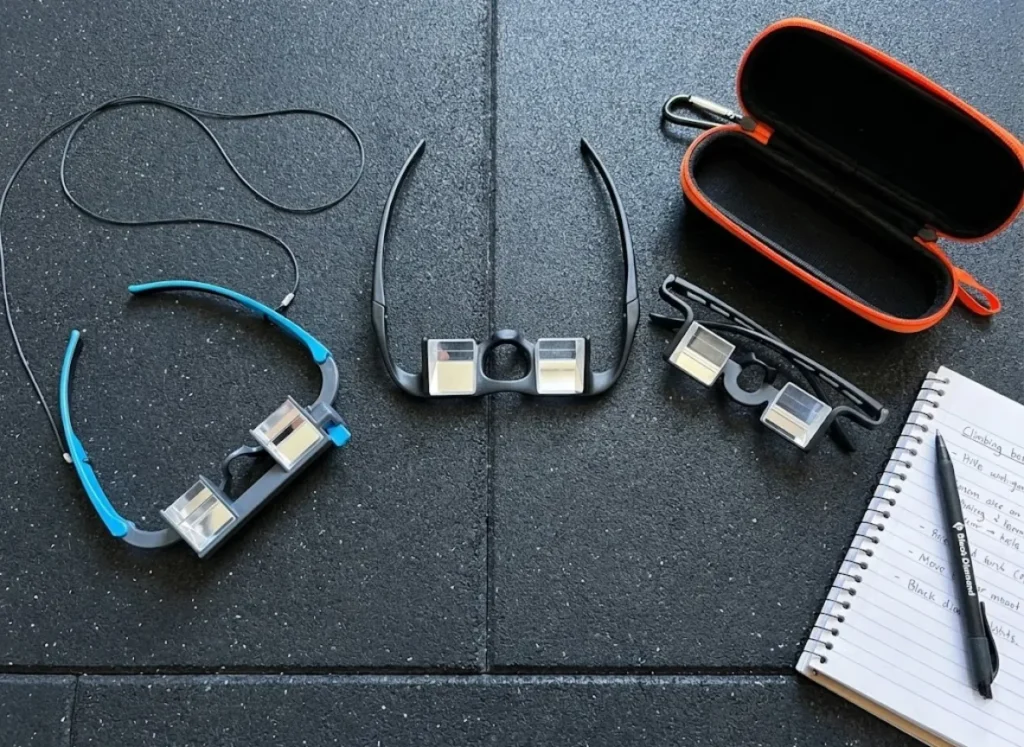 A flat-lay comparison of PitchSix, Metolius, and Y&Y belay glasses arranged on a gym floor for testing and evaluation.