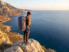 The Solo Readiness Matrix: Best Climbing Styles for Travelers A solo climber with a large haul bag overlooking a limestone coastline at sunset, representing the freedom of unpartnered travel.