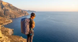 The Solo Readiness Matrix: Best Climbing Styles for Travelers A solo climber with a large haul bag overlooking a limestone coastline at sunset, representing the freedom of unpartnered travel.