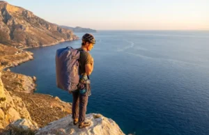 The Solo Readiness Matrix: Best Climbing Styles for Travelers A solo climber with a large haul bag overlooking a limestone coastline at sunset, representing the freedom of unpartnered travel.