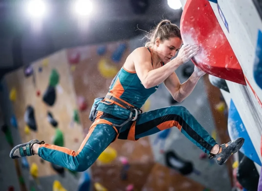 A professional competition climber frozen in mid-air performing a dynamic coordination move on an indoor bouldering wall.