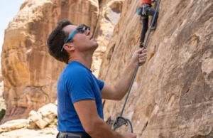 Stop Neck Pain: Best Belay Glasses for Gym Parents A fit parent in a climbing gym belaying comfortably while wearing PitchSix belay glasses, looking up without neck strain, wearing Arc'teryx gear.