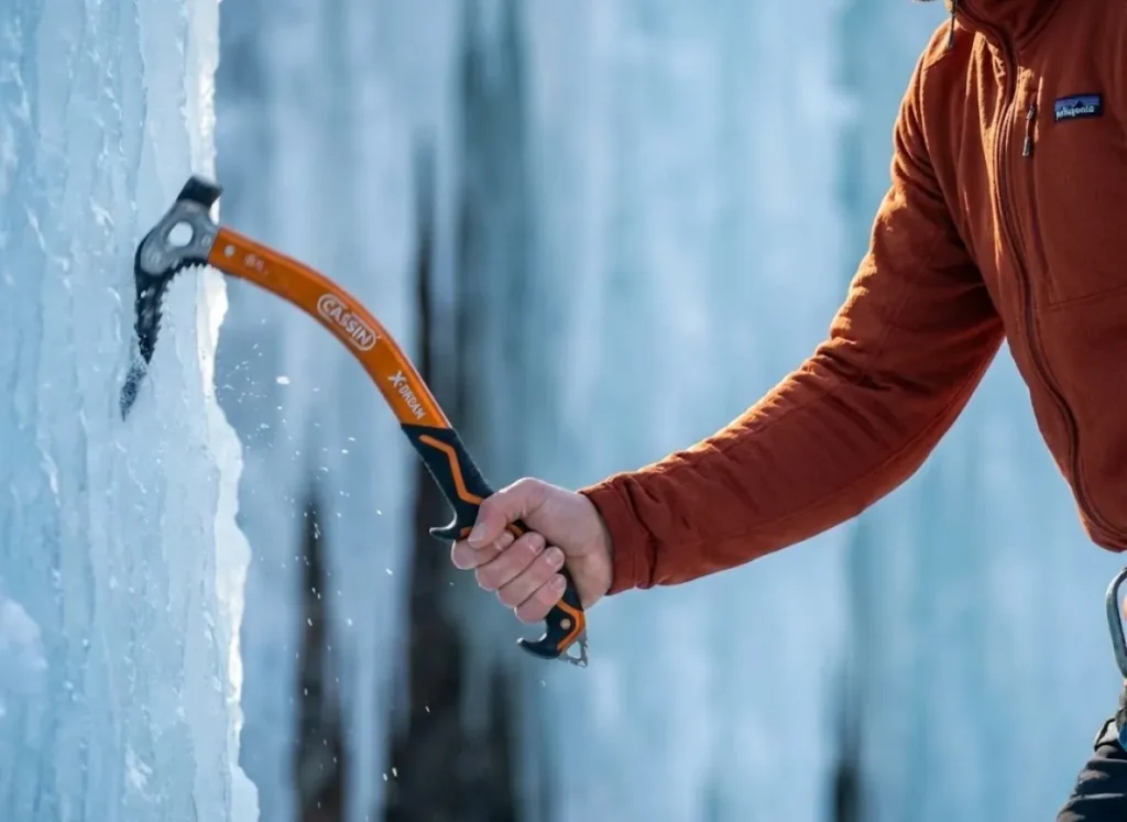 High-speed photography of an ice climber's arm in mid-swing, highlighting the biomechanics and velocity of the Cassin X-Dream tool against a blurred ice background.