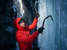 Why Cold Ice Shatters: Brittle Fracture Mechanics Guide A professional ice climber in Arc'teryx gear scaling a brittle blue ice pillar in a frozen canyon, illuminated by a shaft of cold sunlight highlighting the texture of the frozen waterfall.