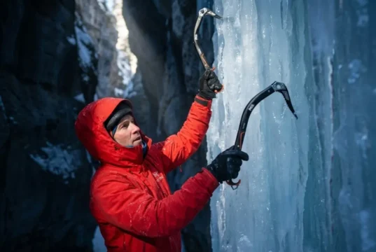 Why Cold Ice Shatters: Brittle Fracture Mechanics Guide A professional ice climber in Arc'teryx gear scaling a brittle blue ice pillar in a frozen canyon, illuminated by a shaft of cold sunlight highlighting the texture of the frozen waterfall.