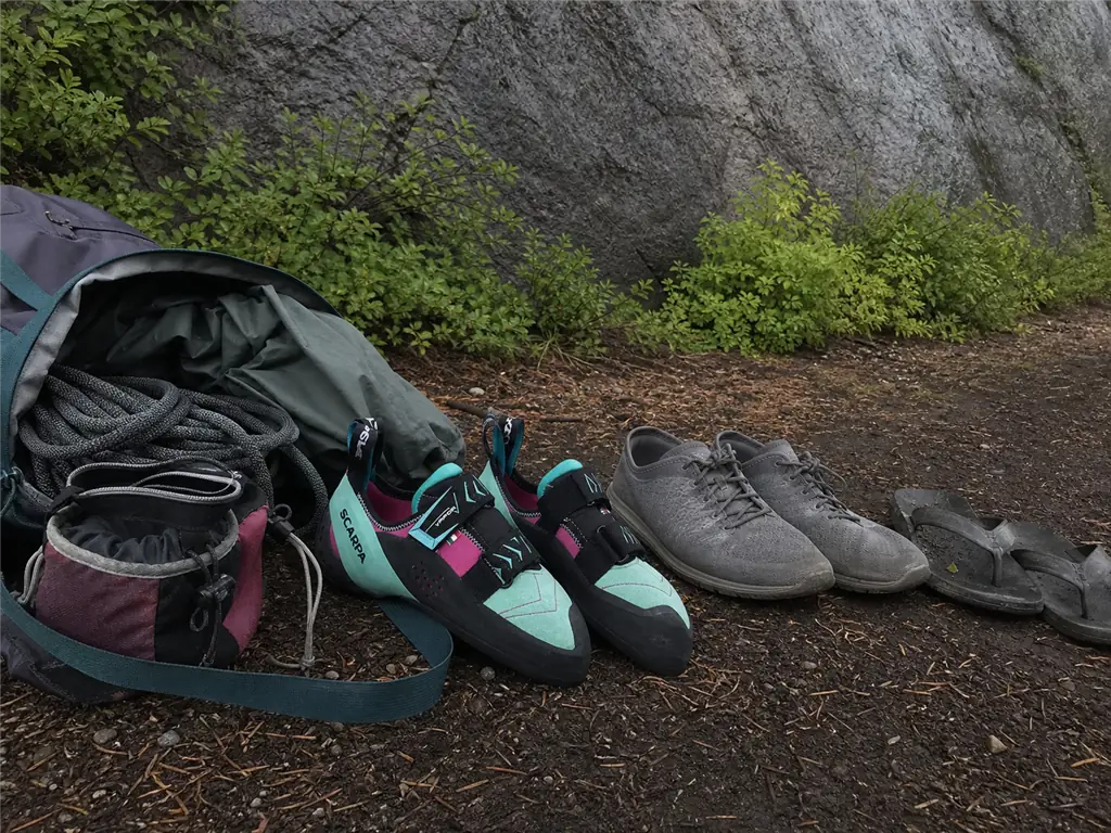 Two pairs of climbing shoes and approach sandals beside an open pack, the two-shoe quiver that protects downturn