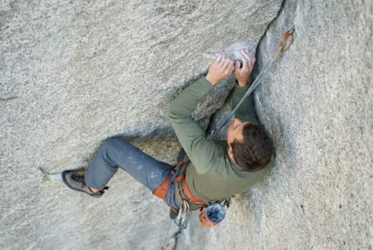 Use Alpine Draws To Reduce Rope Drag Friction Climber on a granite corner route using an alpine draw to straighten the rope path, wearing Arc'teryx gear and using a Mammut rope.