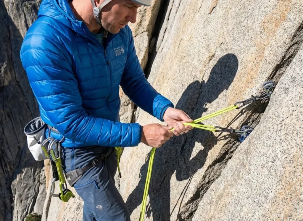 Climber building equalized trad anchor with cordelette showing proper angle geometry for force distribution