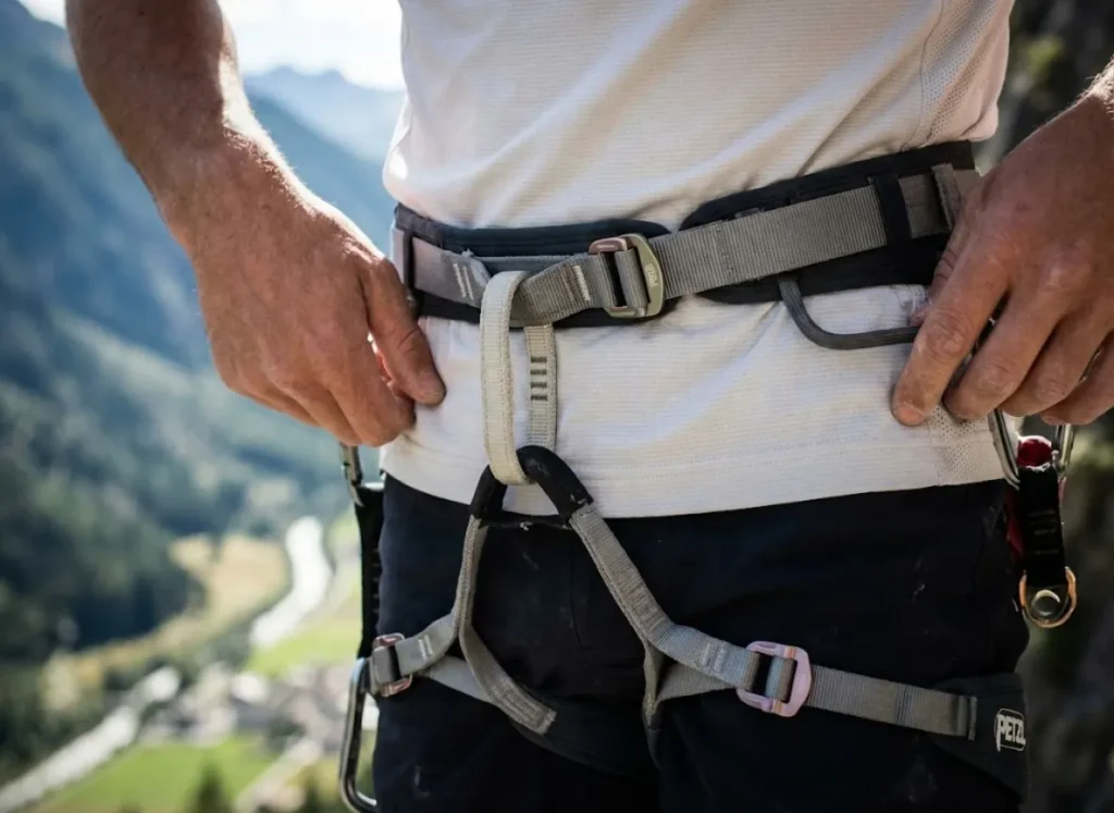 Close-up detail of a Petzl climbing harness waist belt sitting securely above the hip bone (iliac crest) while under suspension tension.