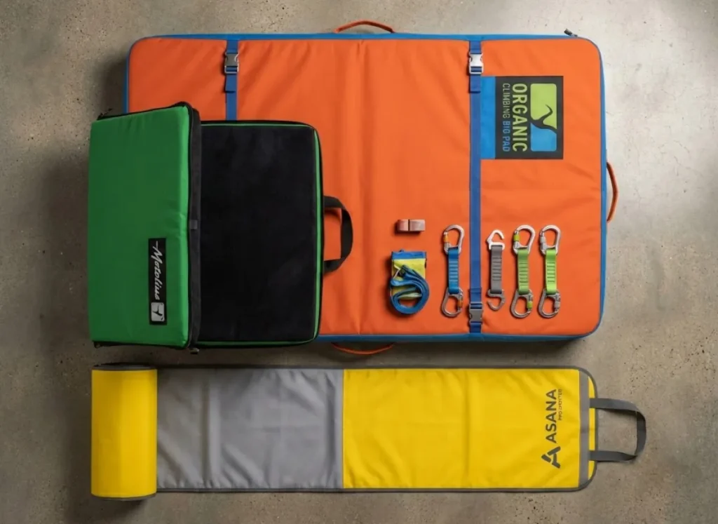 Overhead knolling photography of a complete crash pad system, featuring an Organic Climbing base pad, Metolius satellite pad, and Asana blubber pad arranged on a clean surface.