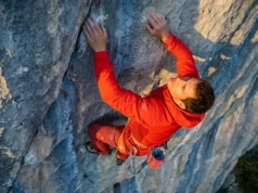 Clip Bolts At The Waist For Maximum Efficiency A professional climber on a limestone wall executing a perfect waist-level clip with a red rope into a silver quickdraw, wearing Arc'teryx gear in golden hour lighting.