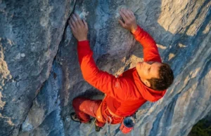 Clip Bolts At The Waist For Maximum Efficiency A professional climber on a limestone wall executing a perfect waist-level clip with a red rope into a silver quickdraw, wearing Arc'teryx gear in golden hour lighting.